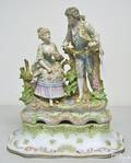 Porcelain statue of young couple in a garden by a fence on a platform
