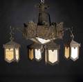 Arts and crafts iron chandelier with four monk heads and four hanging lanterns in hammered pattern lined in caramel slag glass complete with faceted ceiling cap and partial chain unsigned 22 12