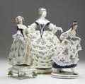 Three porcelain figurines 19th20th c colonial lady with wide skirt lady holding her dress with capo di monte mark and footed figure with paper label indicating montreuil france 1873 tallest 1