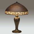 handel table lamp with a brown mosserine shade decorated with floral band over a threesocket bronze base with leaves and buds excellent original patina cap possibly replaced shade stamped handel