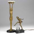 Two art deco nude statues both gilded white metal dancing nymph mounted on a light with a glass ball the other stands with arms stretched upward holding a tray 20th c tallest 23 14