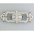 Art deco diamond platinum brooch ca 1935 stirrupform with french cut sapphire accents principal emerald cut diamond approx 50 ct two oec diamonds 66 ct tw smaller oec diamonds 242 cts tw