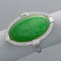 Art deco platinum jade and diamond ring oval jade cabochon 22 x 14 x 6 mm framed by a line of small circular cut and four baguette cut diamonds elaborate scroll pierced gallery and shank with incis