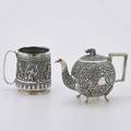 Two indopersian silver vessels spherical teapot with foliate chasings pad feet elephant finial 7 12 across spout footed mug raised with floral and foliate motifs six landscape reserves with f